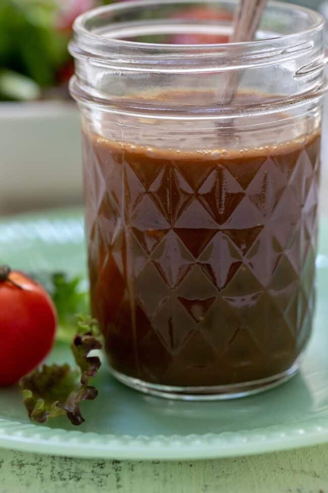 Mason jar filled with oil and seasonings. The jar has a spoon in it and it sits on a green plate.