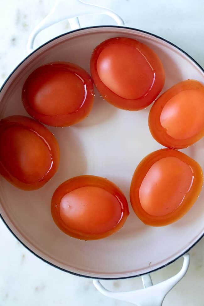 a white pot filled with water and roma tomatoes for blanching, peeling and freezing