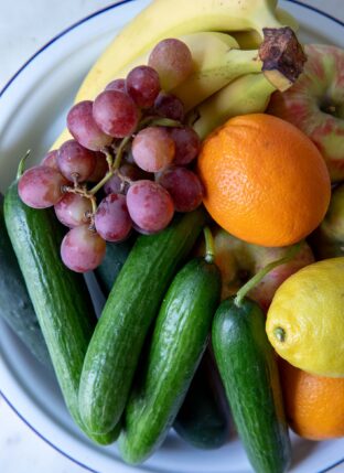 A white bowl filled with fruit and cucumbers