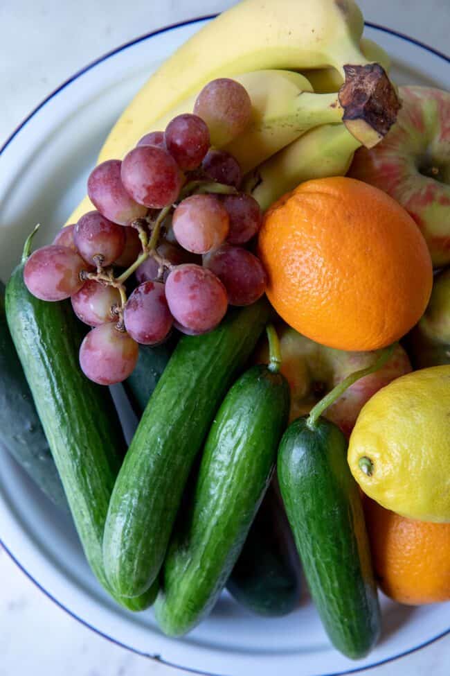 A white bowl filled with fruit and cucumbers