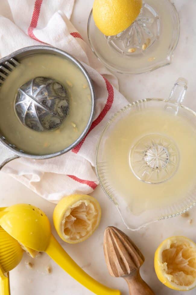 Three hand juicers filled with lemon juice sit next to cut lemon halves (for lemon juice substitutes).