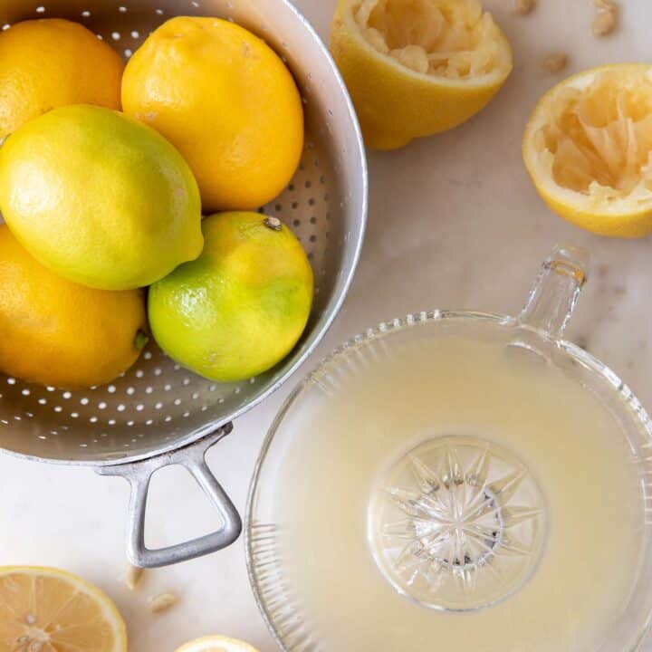 A silver colander filled with lemons. lemons cut in half and juiced in a glass juicer sit next to the colander. For tips and tricks on juicing lemons and how much juice in one lemon