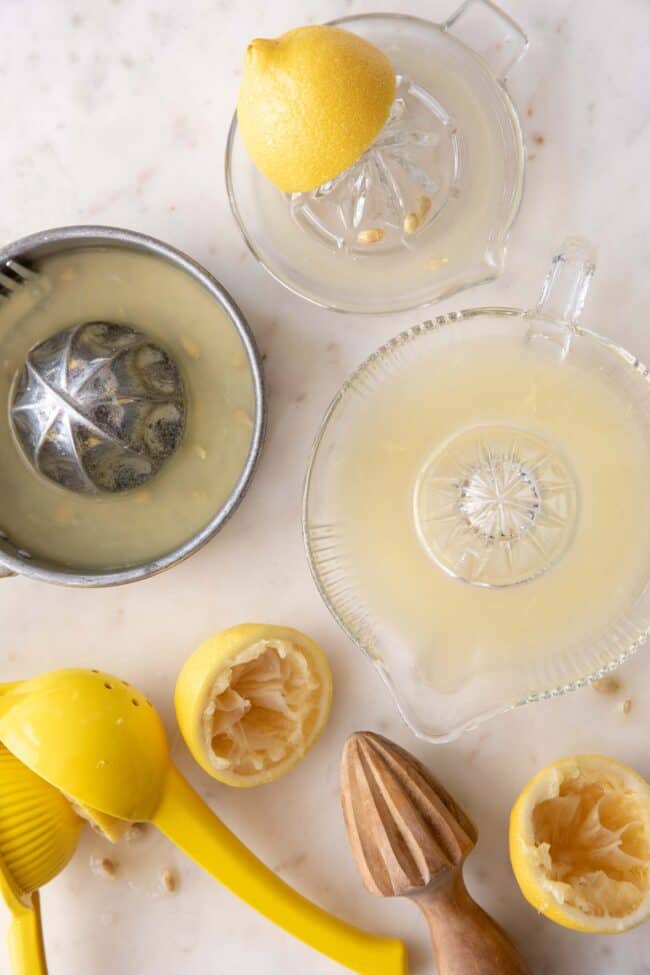 Three hand juicers filled with lemon juice sit next to cut lemon halves (for lemon juice substitutes)