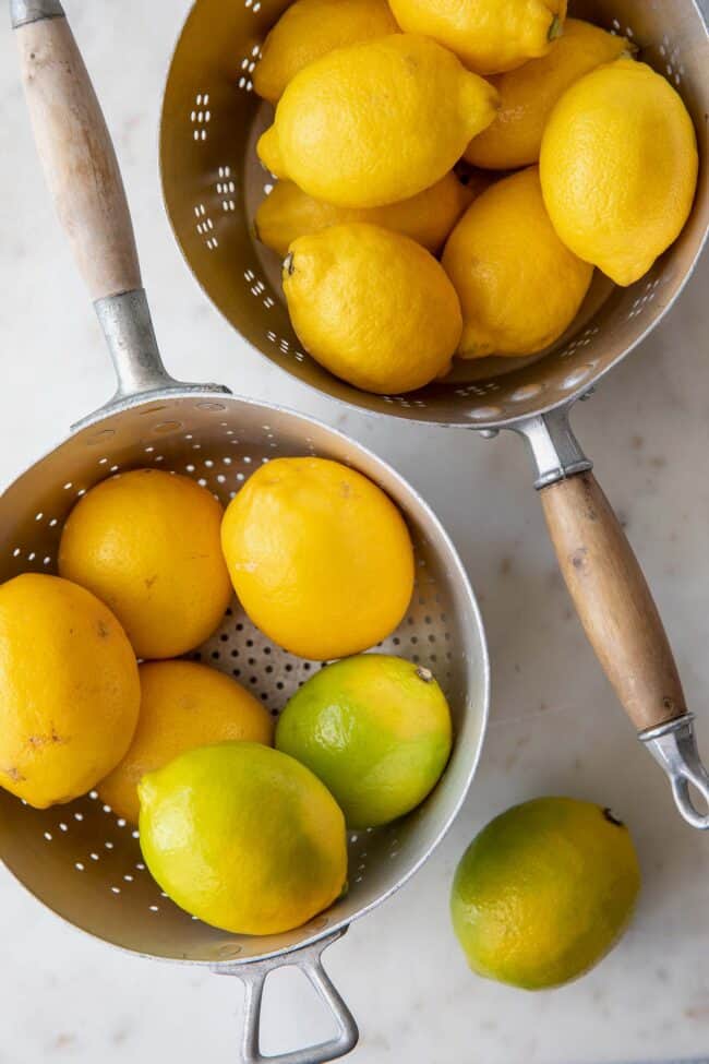 2 silver colanders with wooden handles filled with citrus