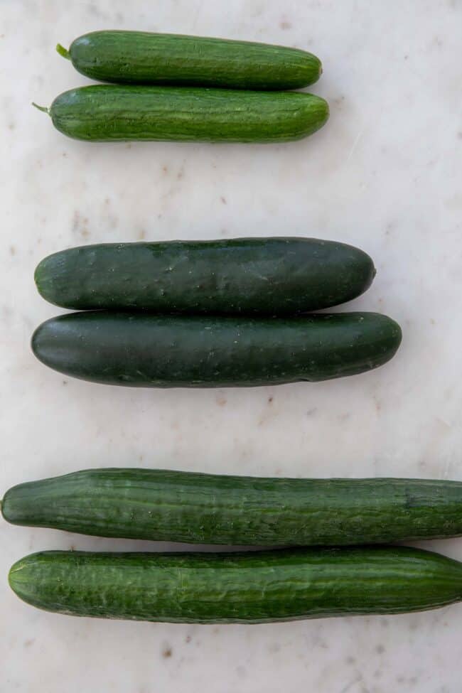 Various types of cucumbers on a white cutting board