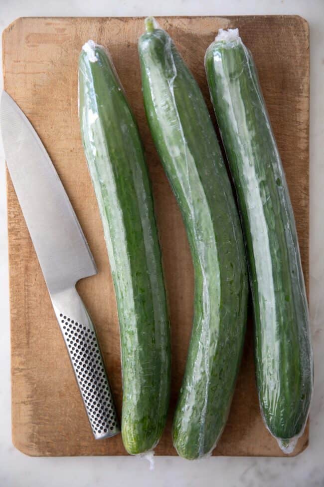 Green fruit sits on a wood cutting board with a knife.