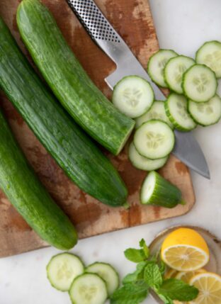 Three English cucumbers and a silver knife sit on a wood cutting board.