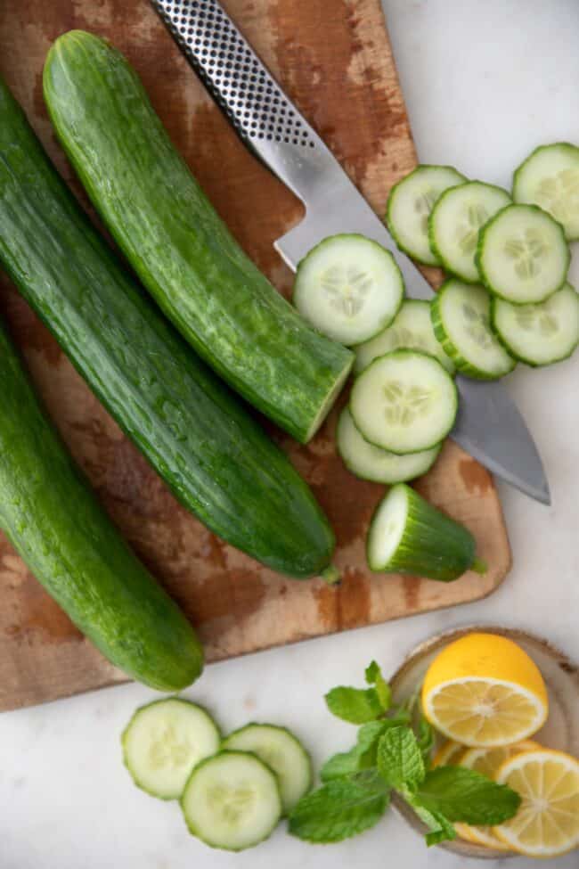 Three cucumbers and a silver knife sit on a wood cutting board