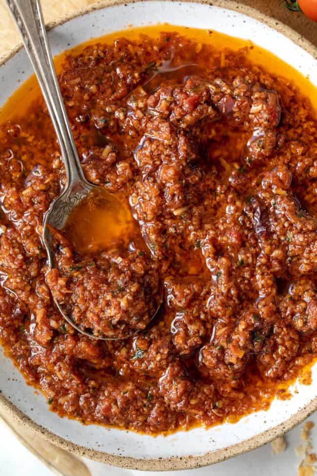 A white bowl filled with red pesto (pesto rosso). A spoon filled with pesto sits in the bowl.