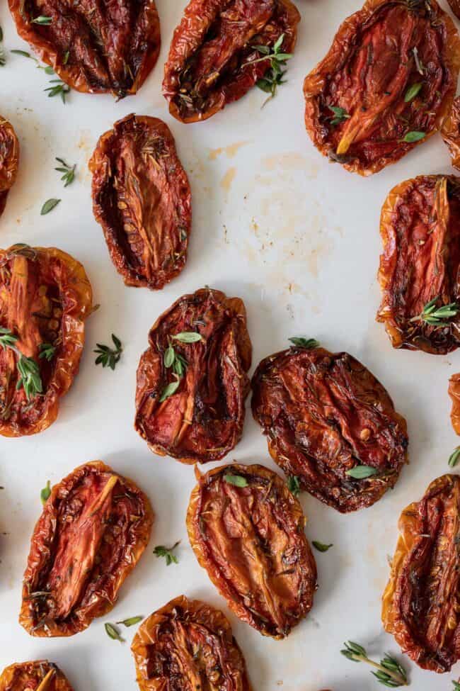 Sun dried tomatoes on a white counter top. The tomatoes are sprinkled with fresh thyme.