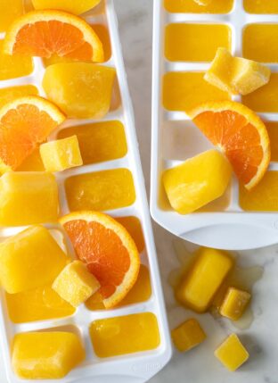 Two white ice cube trays filled with orange ice cubes.