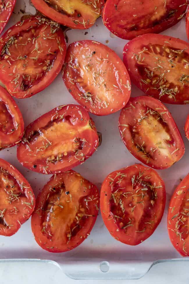 Tomato halves sprinkled with seasoning on a baking sheet.