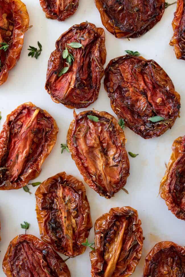 Sliced halves of sun dried tomatoes with fresh thyme leaves sprinkled over them.