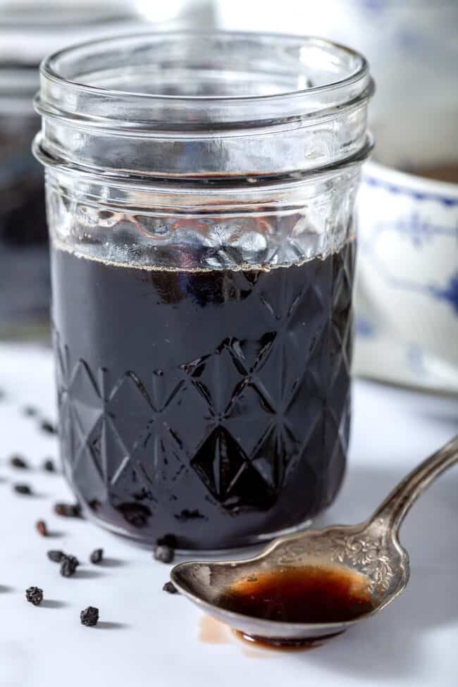 Mason jar filled with elderberry syrup. A spoon filled with the syrup sits next to the jar.