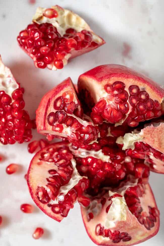 A pomegranate is cut open in 5 sections with some pomegranate seeds scattered next to it.
