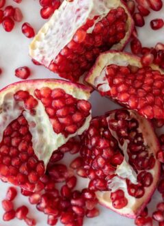 A pomegranate cut into 4 pieces with seeds scattered next to them.