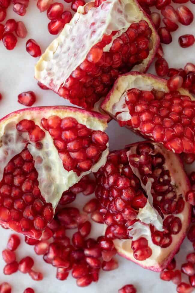 A pomegranate cut into four pieces with pomegranate seeds scattered around it