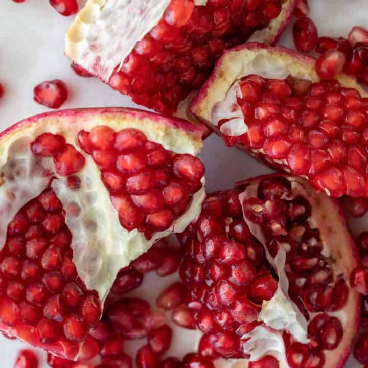 A pomegranate cut into 4 pieces with seeds scattered next to them.