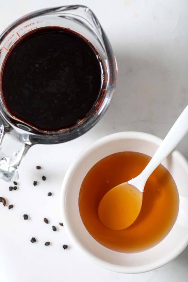 A measuring cup filled with tea and a white bowl filled with honey