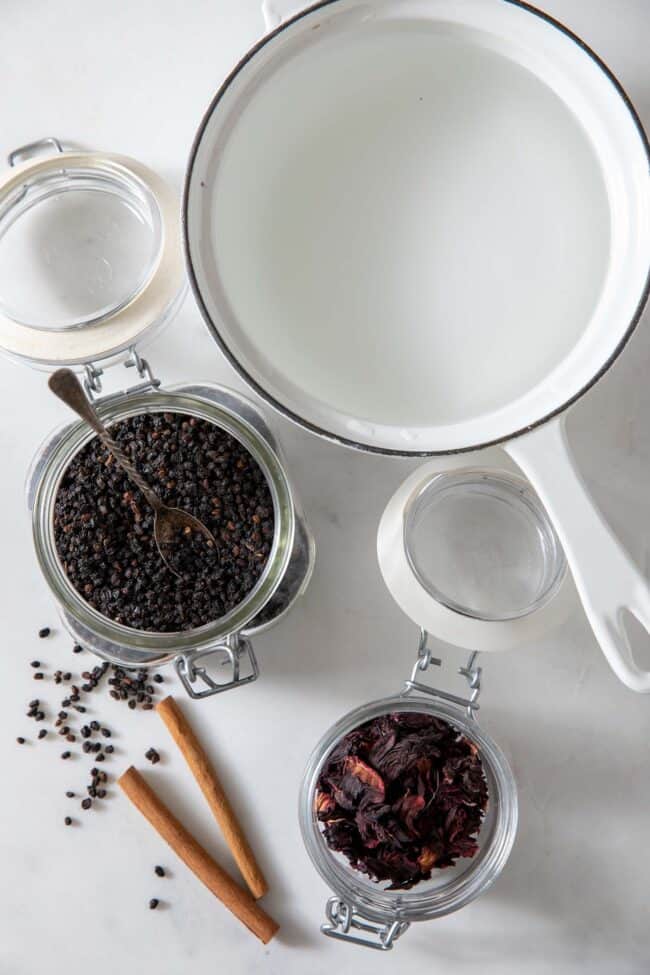 White pot filled with water. Two mason jars filled with dried elderberries and hibiscus