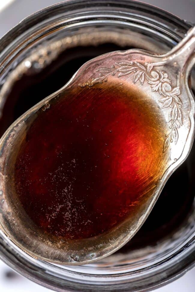 A silver spoon filled with liquid sits on top of a mason jar filled with the same liquid