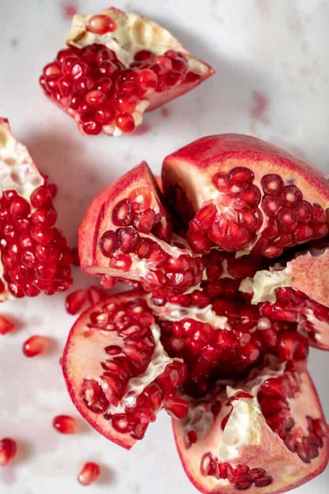 A pomegranate cut into 5 pieces with seeds scattered next to it.