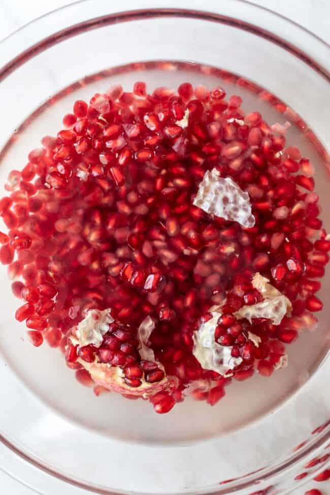 A clear glass bowl filled with water and red arils