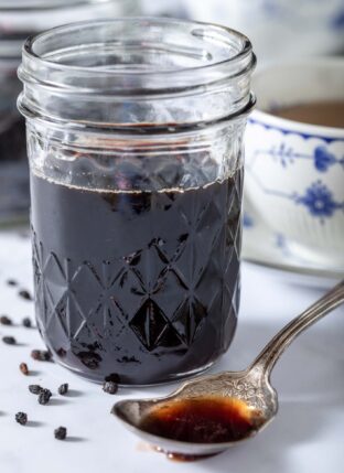 Mason jar filled with elderberry syrup. A spoon filled with the syrup sits next to the jar.