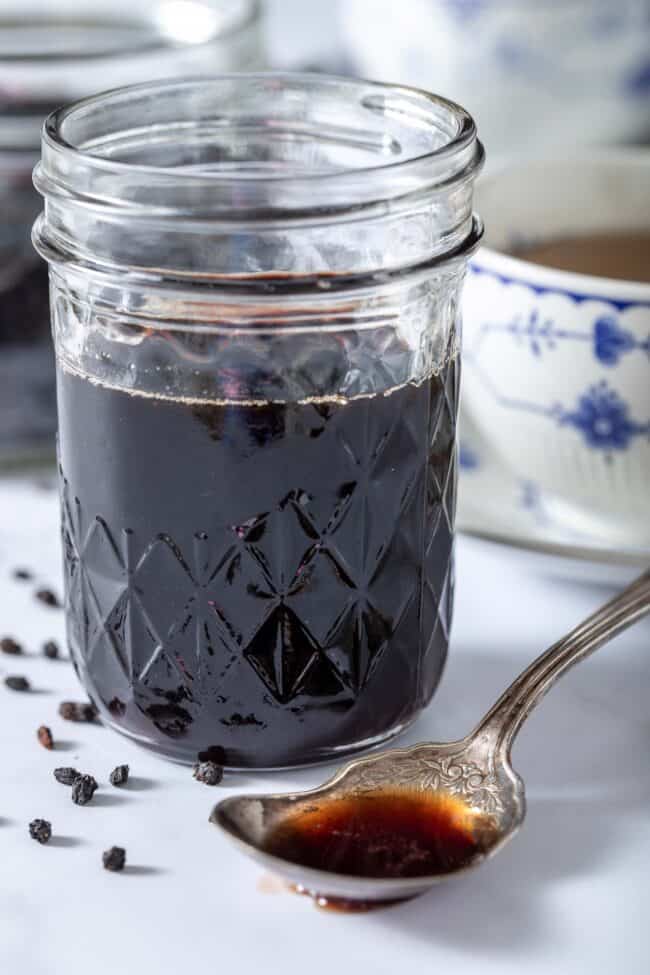 Mason jar filled with elderberry syrup. A spoon filled with the syrup sits next to the jar.