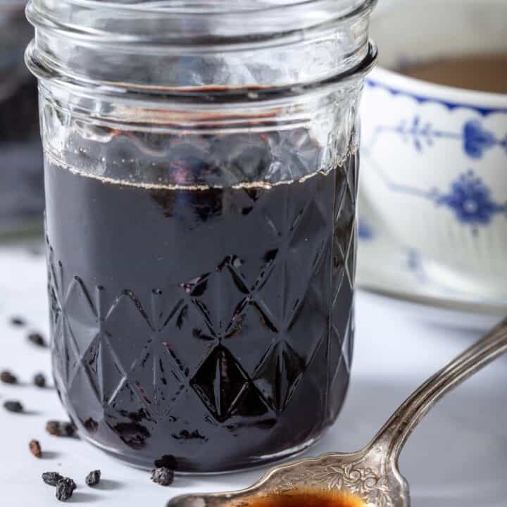 Mason jar filled with elderberry syrup. A spoon filled with the syrup sits next to the jar.