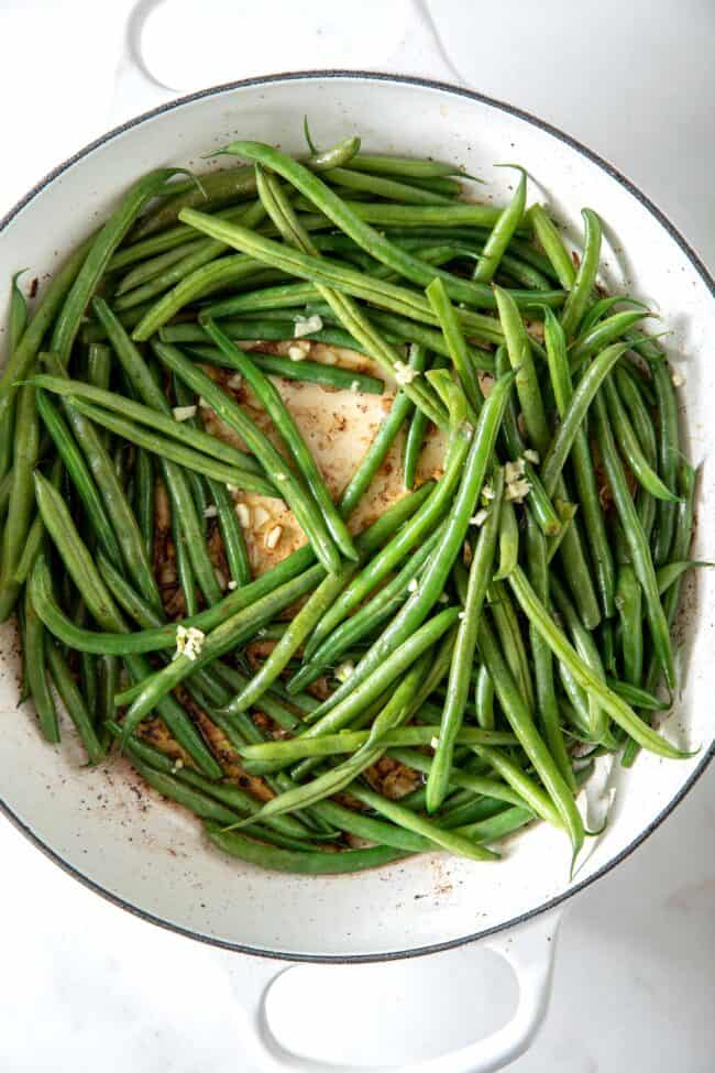 White skillet filled with haricot verts (French green beans) and minced garlic.