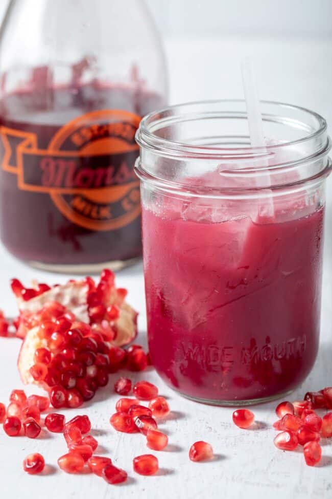 A tall glass bottle and mason jar filled with dark pink fruit extract.