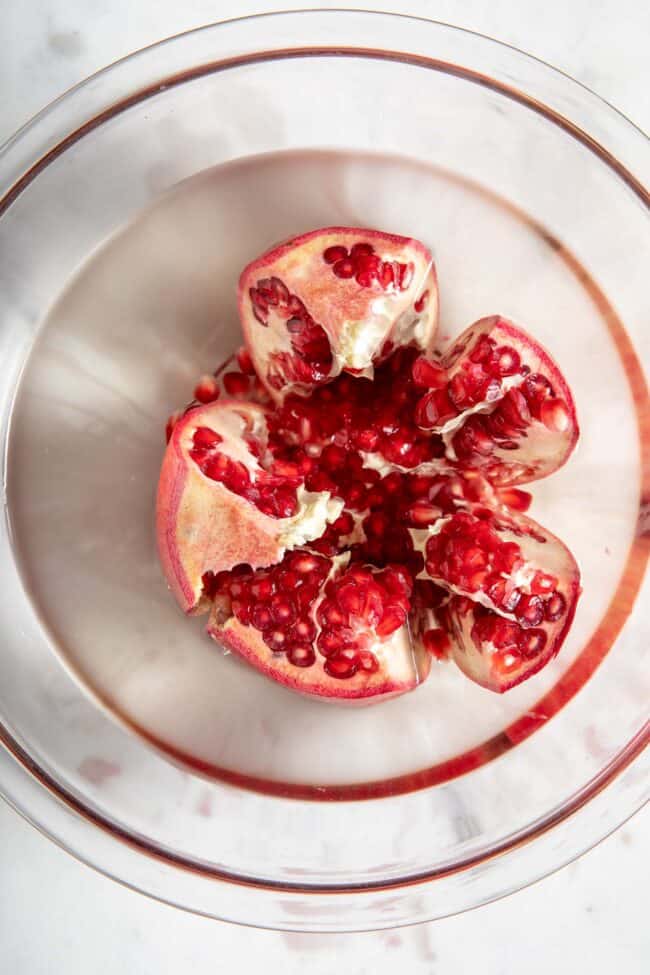 A glass bowl filled with water with a sliced red fruit sitting in the middle of the bowl.