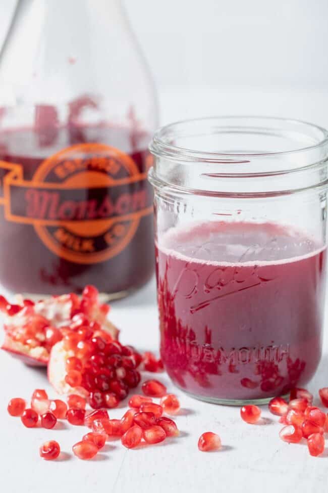 A glass bottle and mason jar filled with dark pink fruit extract.