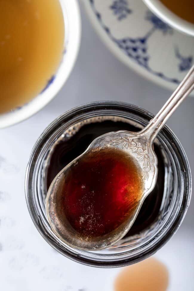 A spoon filled with a liquid sits on top of a mason jar filled with the same liquid.