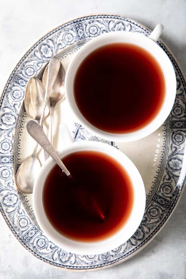 Two white cups of tea sit on a blue and white oval platter