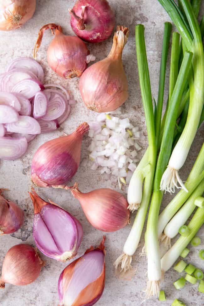 Whole shallots, sliced shallots and minced shallots sit on a counter next to loose green onions