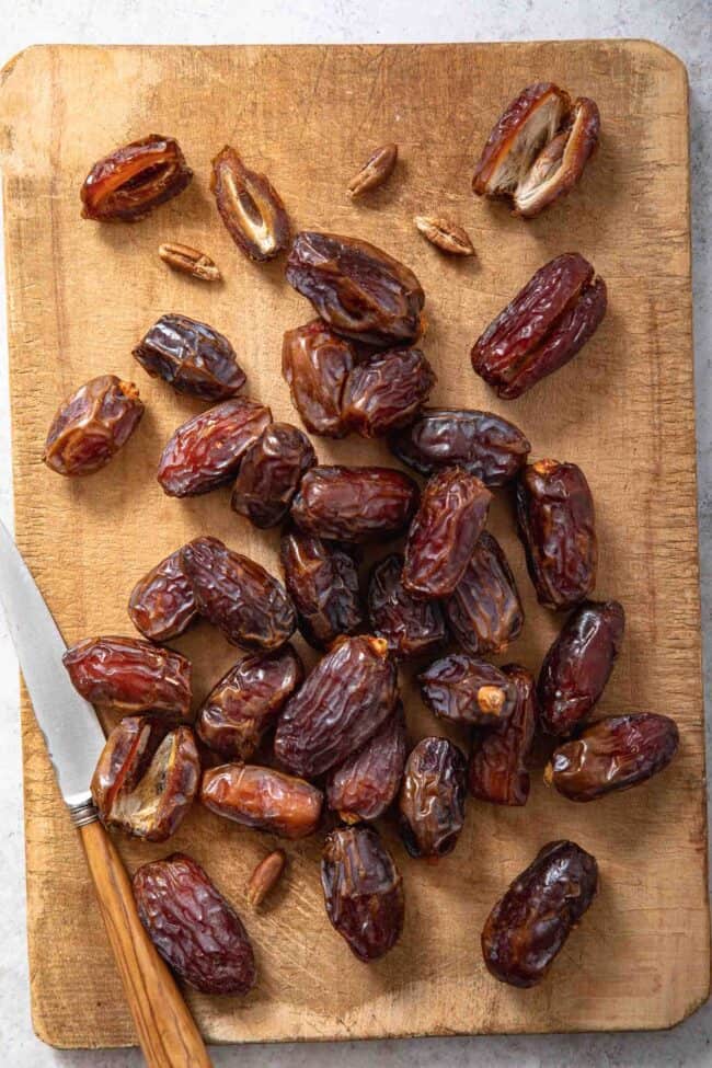 A wood cutting board covered with dates. A knife sits next to the dates on the cutting board.