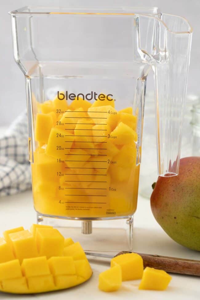 Clear plastic blender pitcher filled with cut mango fruit