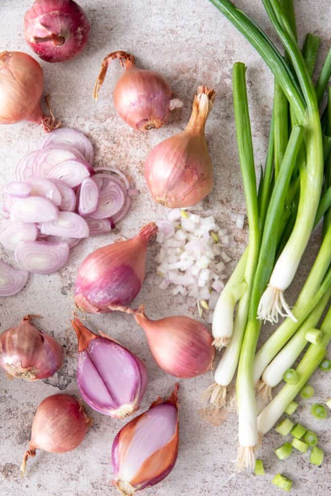 Whole and sliced alliums sit on a counter next to loose green onions