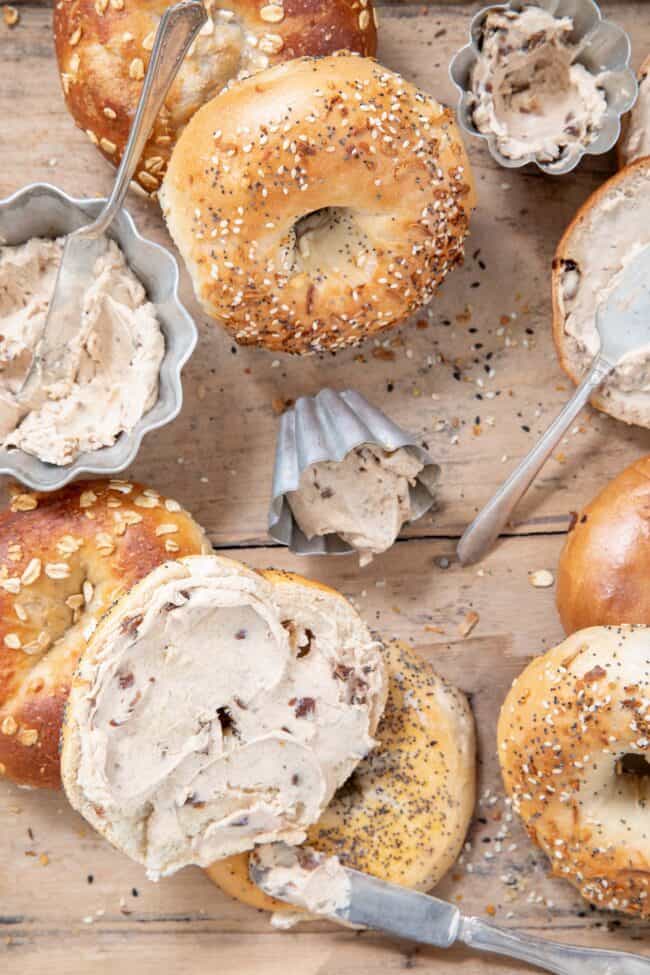 Bagels scattered on a wooden tray with silver ramekins filled with a creamy spread.
