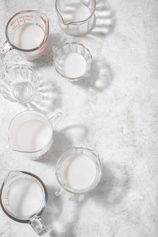 7 clear glass measuring cups filled with almond milk to measure how many cups in a quart