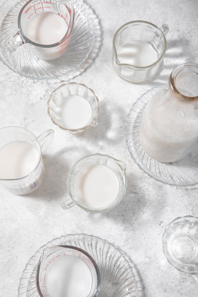 7 clear glass measuring cups and a clear glass quart bottle filled with almond milk