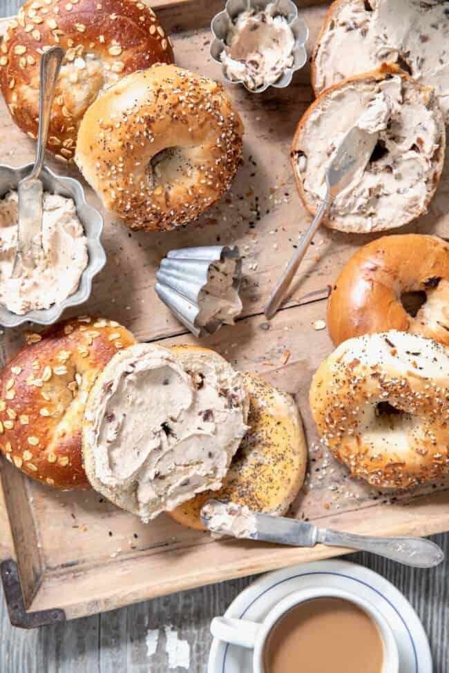 Bagels scattered on a wooden tray with silver ramekins filled with cinnamon raisin cream cheese spread.