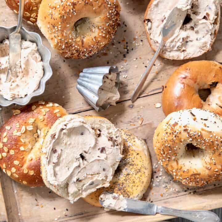 Bagels scattered on a wooden tray with silver ramekins filled with cinnamon raisin cream cheese spread.