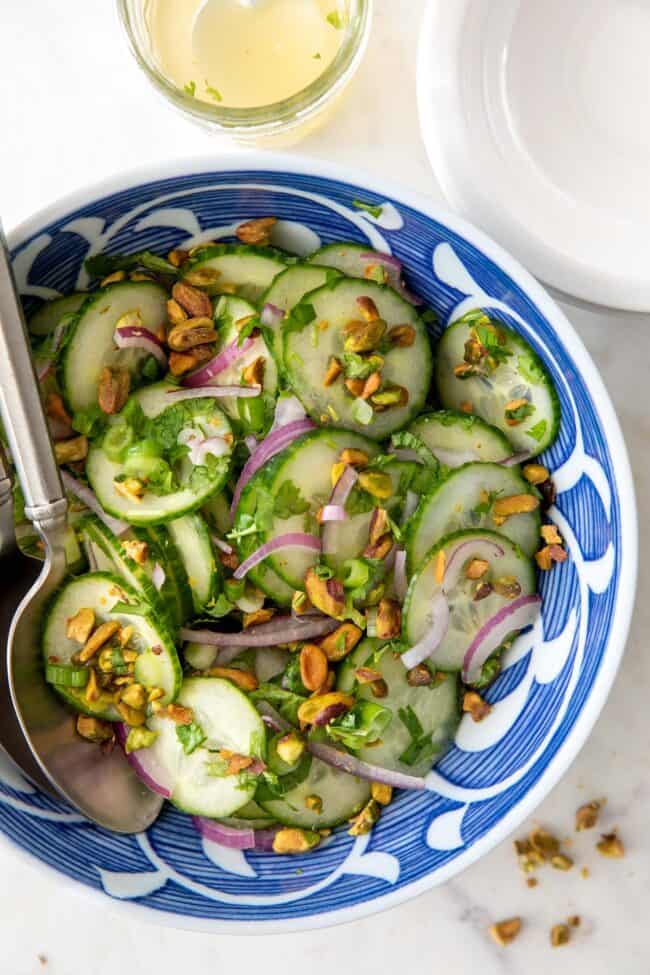 Blue and white bowl filled with Asian cucumber salad. Two silver spoons rest in the bowl.