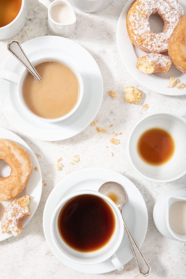 white coffee cups filled with coffee and donuts sitting on white plates with crumbs