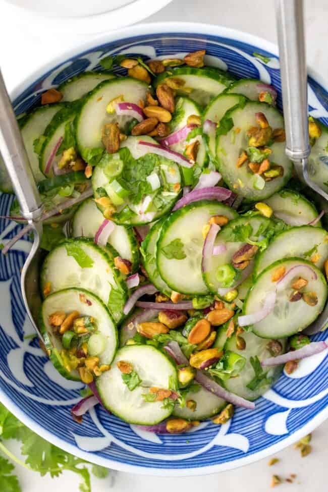 Blue and white bowl filled with Asian cucumber salad with cilantro, pistachios and onion.