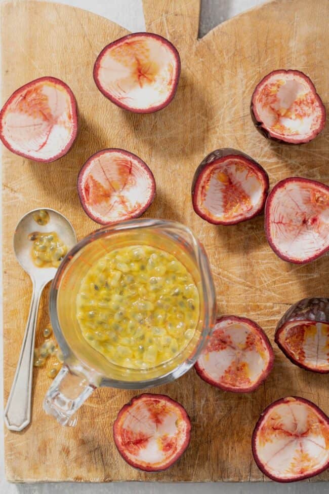 Several pieces of lilikoi on a wooden cutting board. A glass measuring cup is filled with pulp from the fruit.