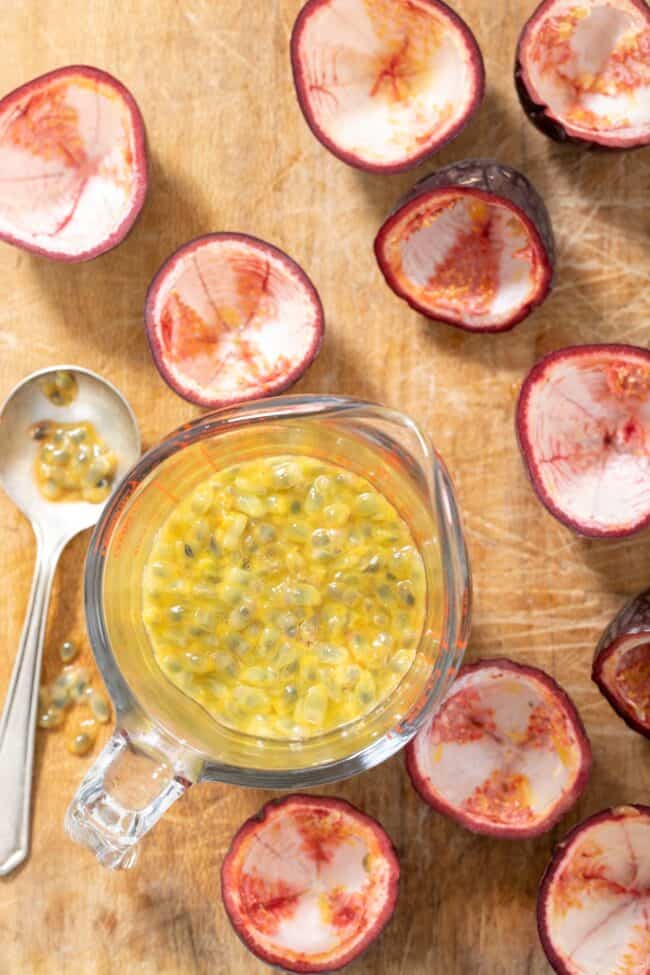 A glass measuring cup filled with fruit pulp. A spoon and cut fruit sits next to the measuring cup.